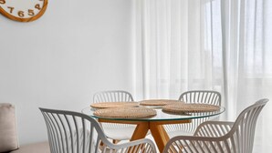 A room with a round glass table surrounded by white chairs, a woven placemat, and a wooden-framed clock on the wall. - Bay View Motel - Sunrise (Lorne)