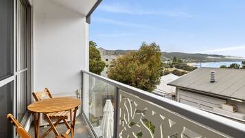A balcony with a wooden table and chairs, overlooking a coastal landscape with buildings and trees.