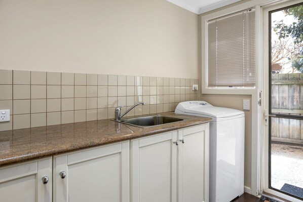 A kitchen with a built-in sink, white cabinets, and a window with blinds.
