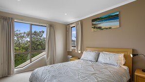 A bedroom with a large bed, a nightstand, a lamp, and a painting on the wall. - Sound Of The Sea (Apollo Bay)