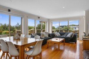 A spacious living area with a dining table, sofas, and large windows offering a view of the outdoors.