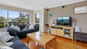 A modern living room with a sofa, a coffee table, a TV, and a bookshelf. - Sound Of The Sea (Apollo Bay)