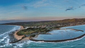 An aerial view of a coastal town with a marina, sandy beaches, and a hilly landscape. - Sound Of The Sea (Apollo Bay)