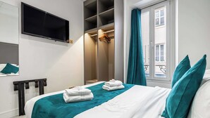 Habitación de hotel con cama, televisor montado en la pared, armario y ventana con cortinas.