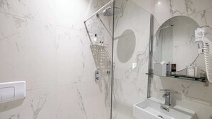 Un baño moderno con ducha de vidrio, lavamanos blanco y espejo con marco redondo.