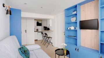 A modern living room with a grey sofa, a small black side table with a plant, and a blue shelving unit with a TV.