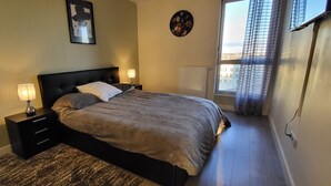 A bedroom with a bed, two bedside tables with lamps, a radiator, and a window with curtains. - Luxury apartment (Lille)