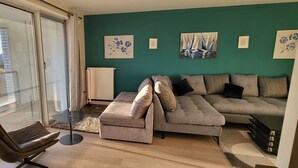 A modern living room with a sofa, a chair, and a table. There are paintings on the wall and a view of the outside through a window. - Luxury apartment (Lille)