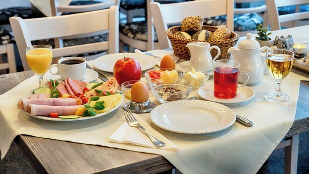 Uma mesa de café da manhã com pratos de comida, um jarro de café, um copo de suco de laranja e uma chaleira.