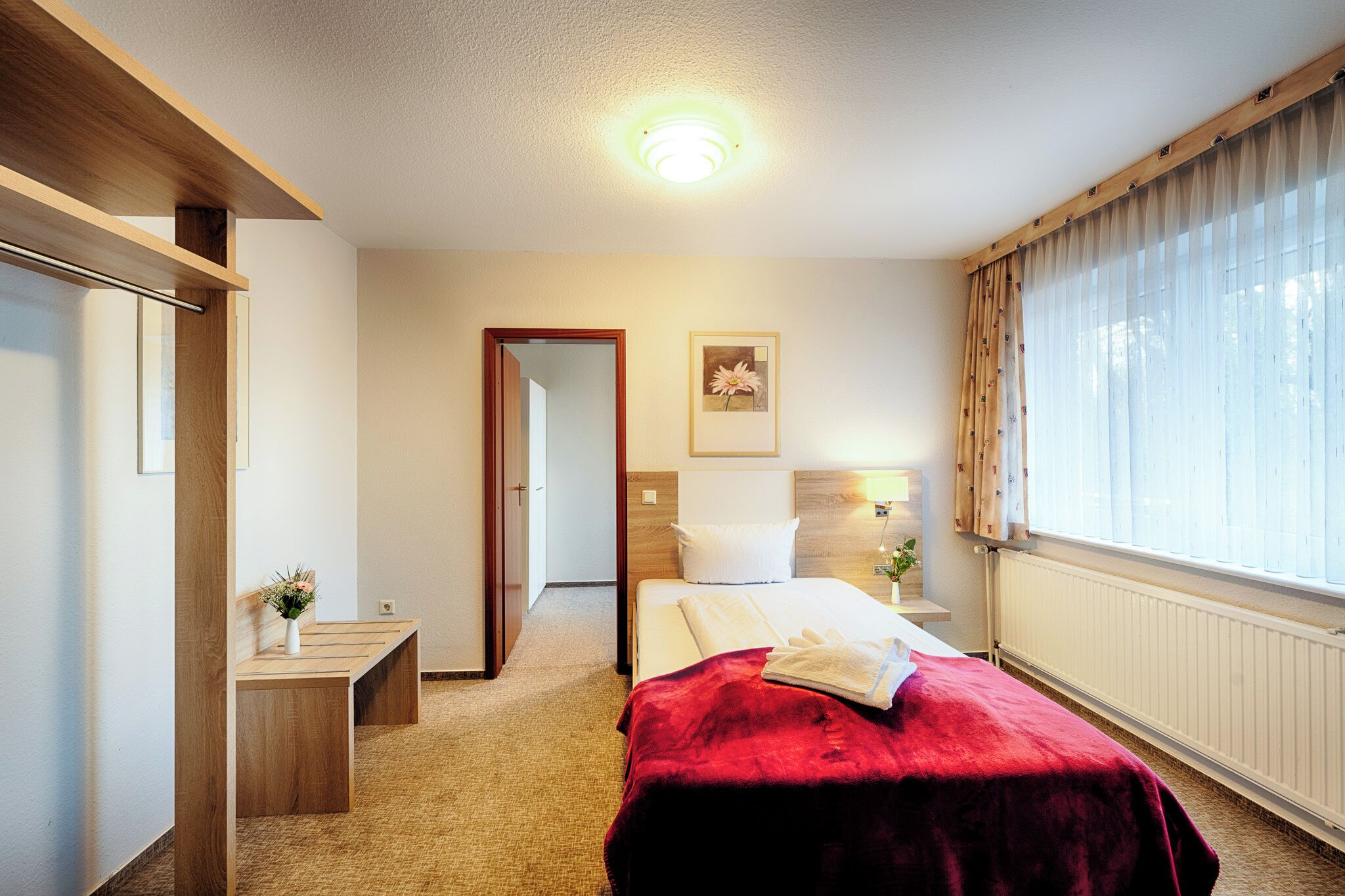 Et hotelværelse med seng, natbord, lampe og udsigt til det fri gennem et vindue.