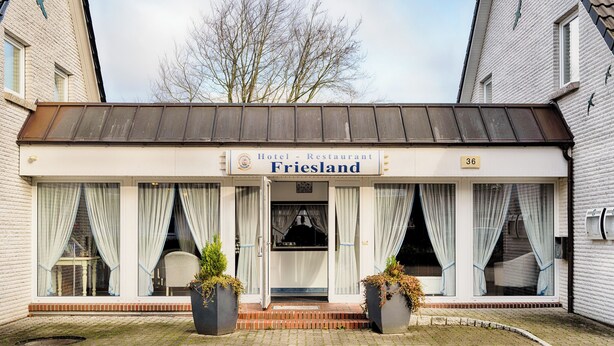 A hotel named 'Friesland' with a sign above the entrance, a brick facade, and large windows with curtains. - Hotel Friesland  (Leck)