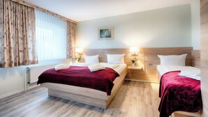 Quarto de hotel com uma cama grande, uma cama menor e uma mesa de cabeceira com abajur.