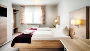 A hotel room with a bed, bedside tables, a TV, a window with curtains, and a lamp. - Hotel Friesland  (Leck)