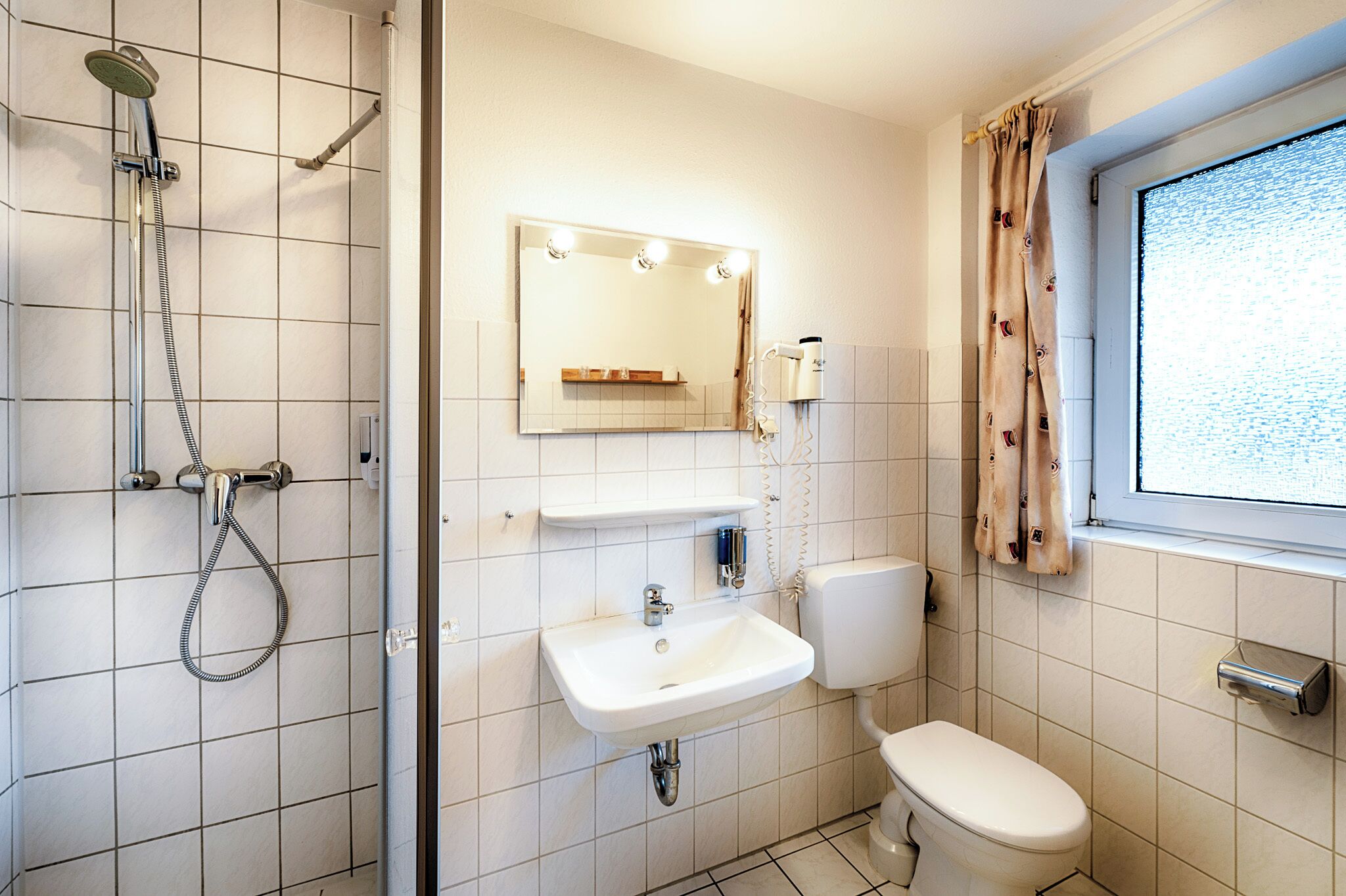 Un baño con ducha, lavabo, inodoro y una ventana con cortinas.