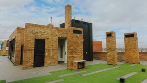 Un edificio moderno con ladrillo y paneles negros, una chimenea y un pequeño espacio exterior con césped artificial.