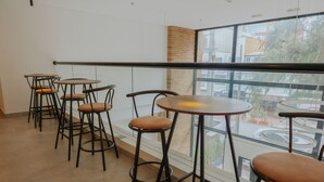 Un interior moderno con mesas altas y taburetes, ventanas amplias con vistas a la calle y una pared de ladrillo decorativa.