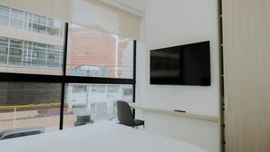 Una habitación de hotel moderna con un ventanal grande, un televisor de pantalla plana en la pared y un escritorio pequeño con una silla.