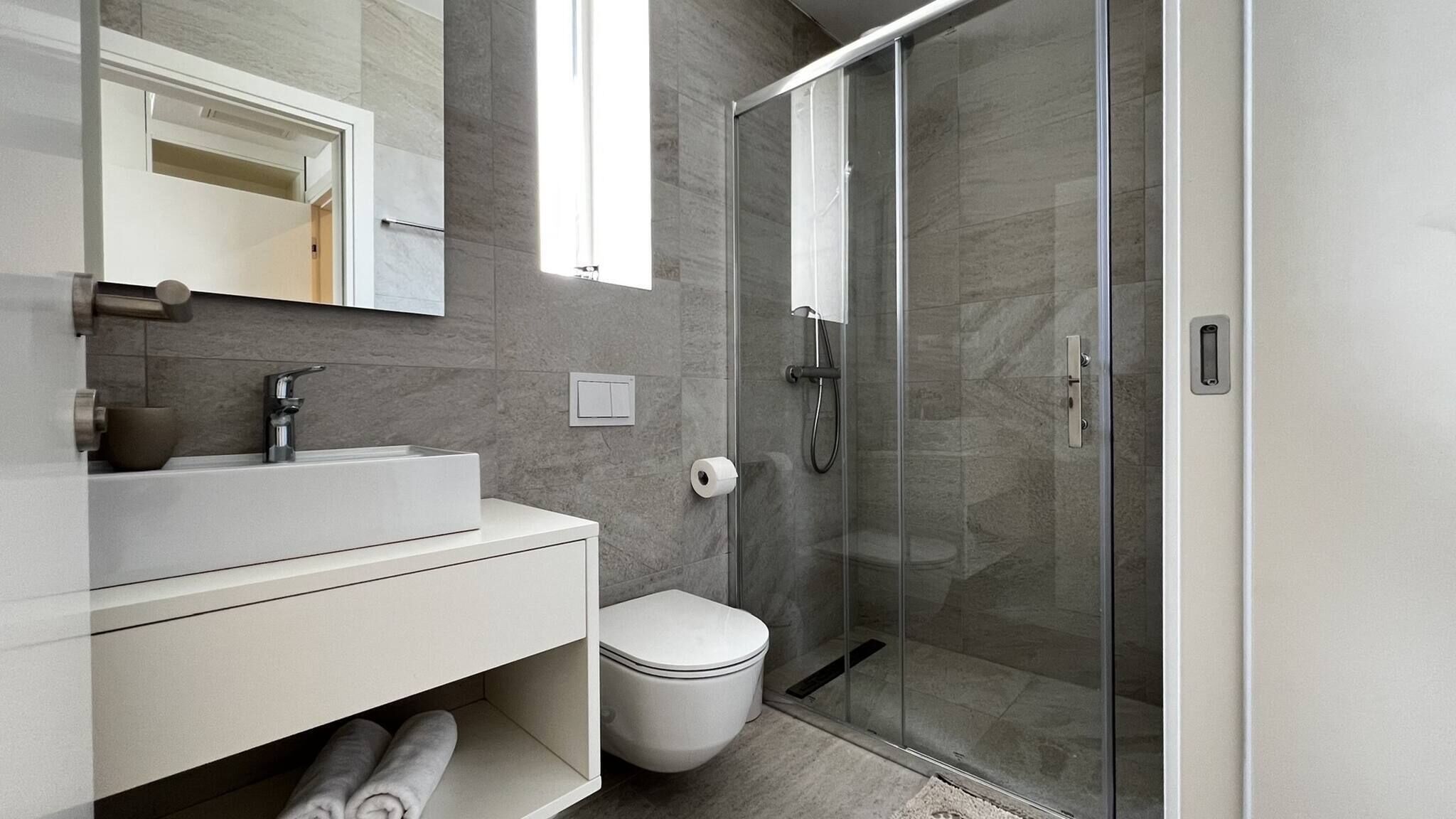 A modern bathroom with a glass-enclosed shower, a white sink, and a toilet.