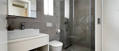 A modern bathroom with a glass-enclosed shower, a white sink, and a toilet.