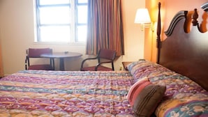 Habitación de hotel con una cama grande, una mesa redonda, dos sillas, una lámpara y una ventana con cortinas.
