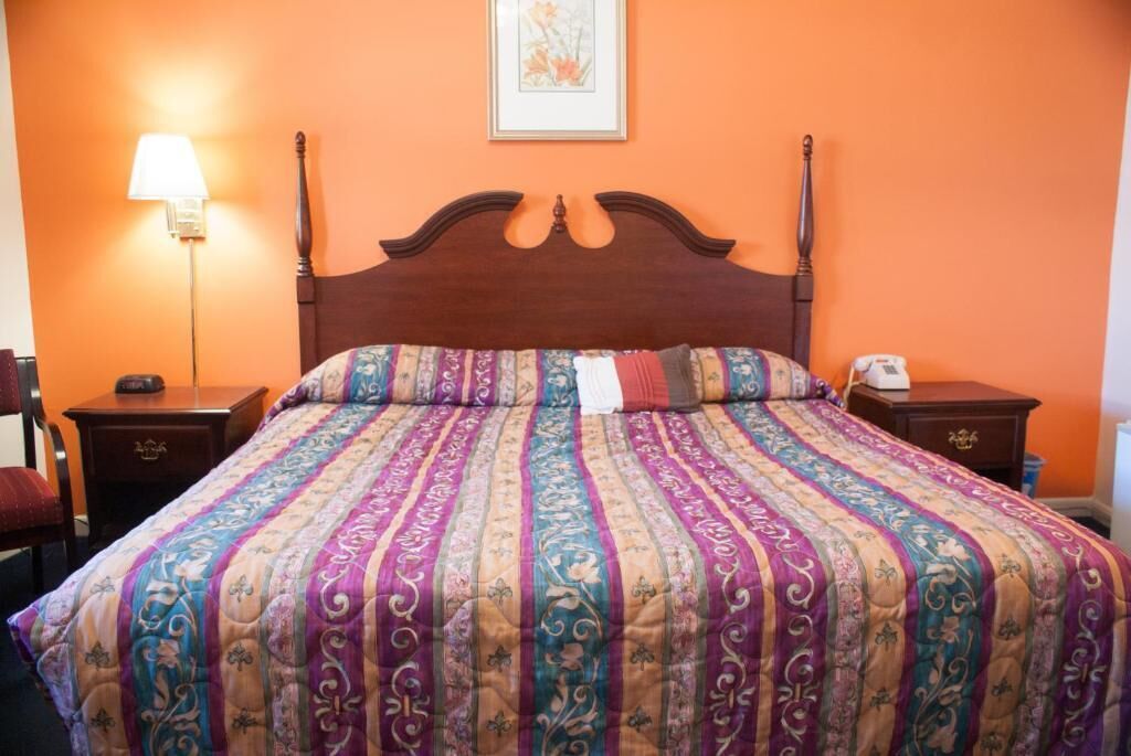A bed with a patterned bedspread, a wooden headboard, a bedside lamp, and a nightstand with a phone.
