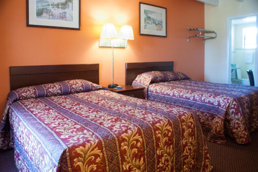 Een hotelkamer met twee bedden, elk voorzien van beddengoed met een patroon, een nachtkastje, een lamp en ingelijste foto’s aan de muur.
