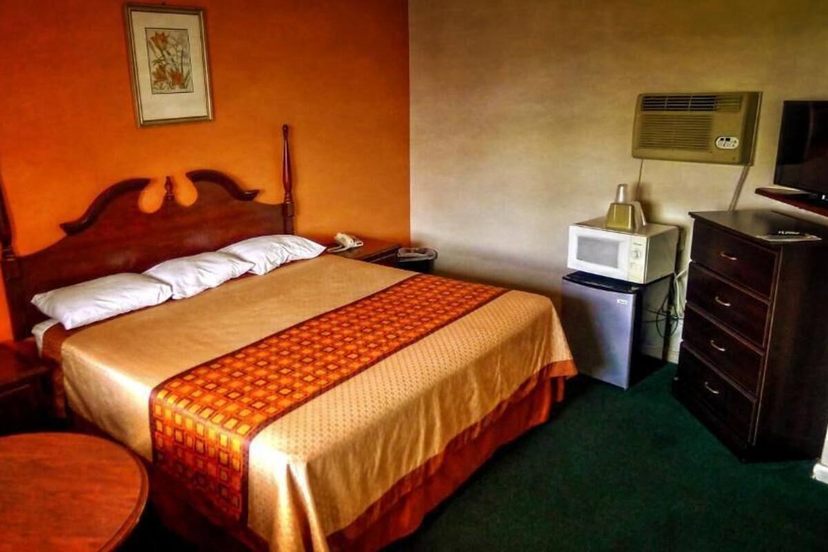 A hotel room with a wooden bed, a desk with a lamp, a microwave, and a TV.