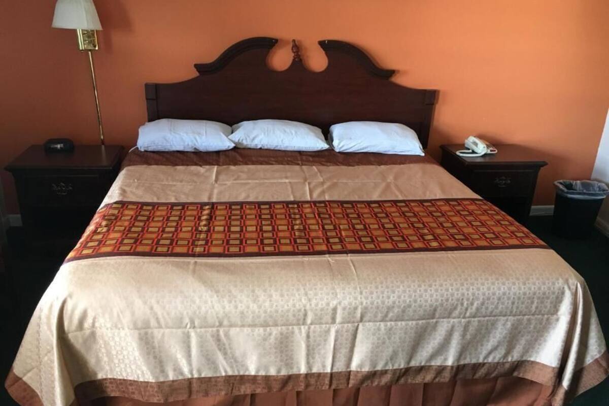 A neatly made bed with a patterned bedspread, two bedside tables with lamps, and a trash bin.