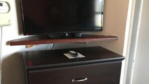 Un mueble de madera oscura con un televisor de pantalla plana encima, un control remoto y una tarjeta pequeña.