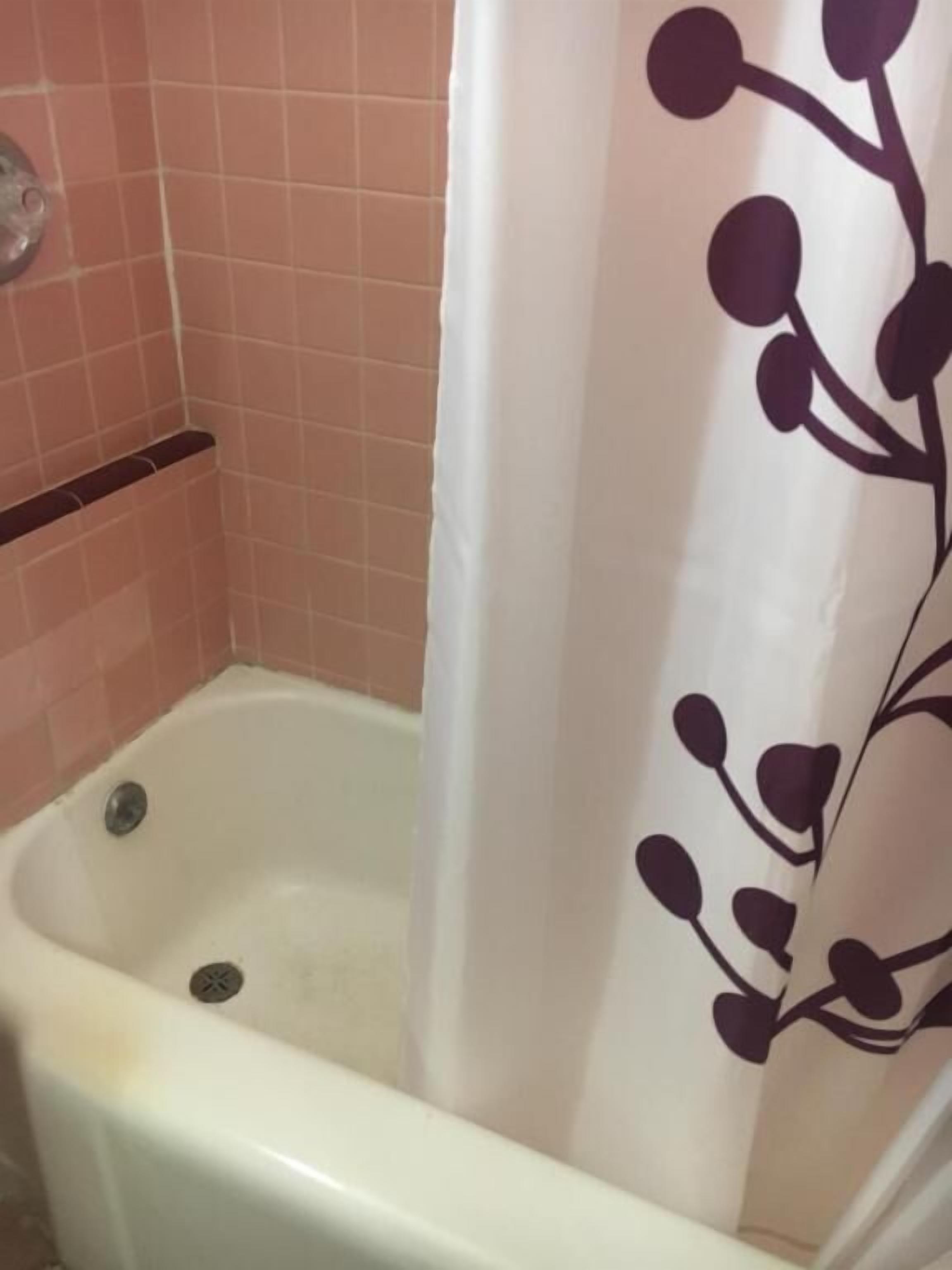 A bathtub with a white shower curtain featuring a dark floral pattern.