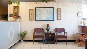 Un área de recepción con dos sillas de madera, una mesita con un florero y un mapa en la pared.