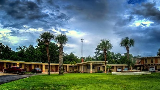 Un motel con césped, palmeras y cielo despejado.