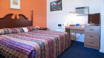 A bedroom with a large bed, a desk with a computer, a dresser, and an air conditioner.