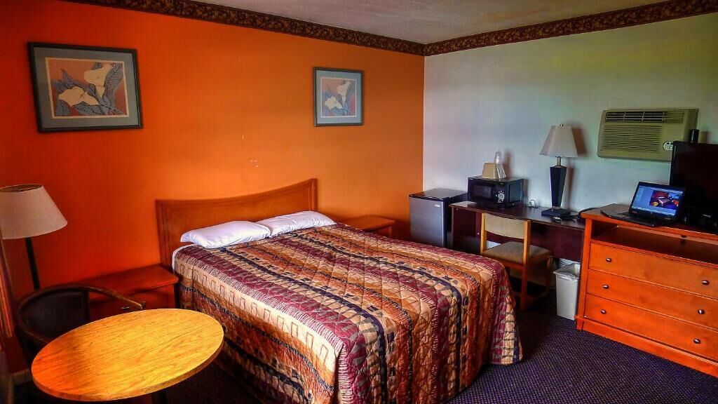 A hotel room with a bed, a desk with a computer, a chair, a dresser, and a small round table.