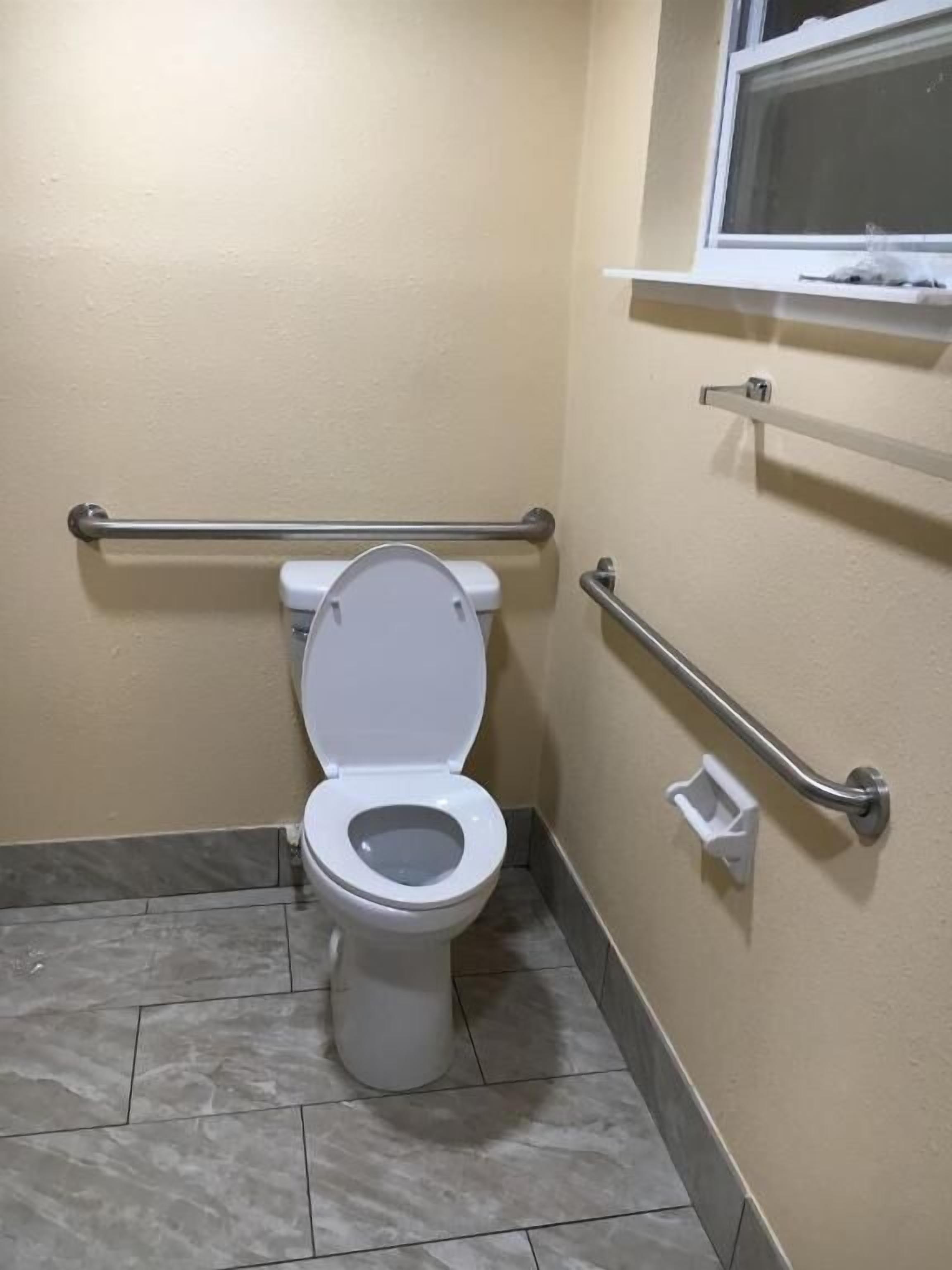 A bathroom with a white toilet, grab bars, and a window above the toilet.