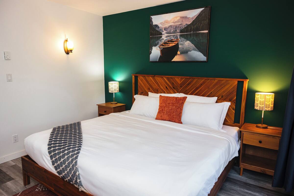 A neatly made bed with white linens and a patterned throw, a wooden headboard, and two bedside lamps.