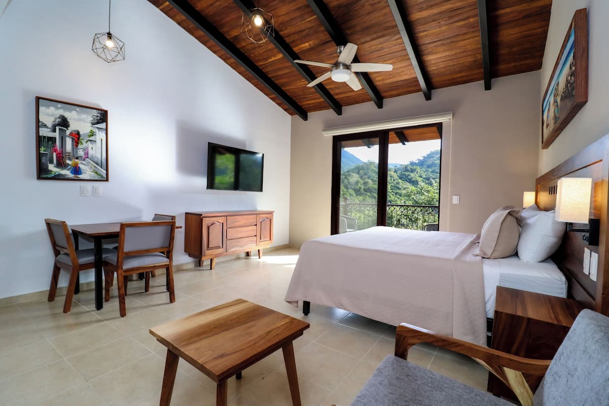 A bedroom with a bed, a desk, and a chair. There is a window with a view of greenery.