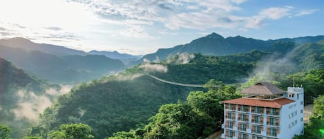 Un hotel con techo rojo, rodeado de montañas verdes exuberantes y una carretera serpenteante.