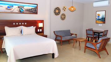 A hotel room with a bed, a sofa, a dining table with chairs, and decorative wall art.
