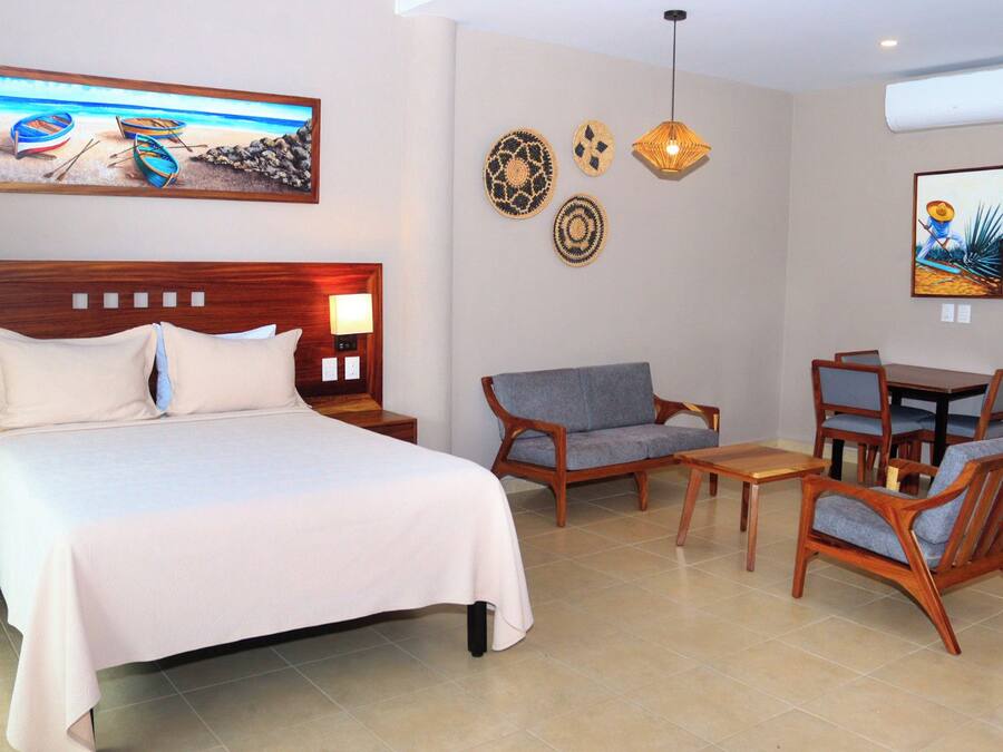 A hotel room with a bed, a sofa, a dining table with chairs, and decorative wall art.