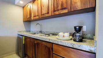 Una cocina con gabinetes de madera, encimera de granito, lavavajillas de acero inoxidable y cafetera.