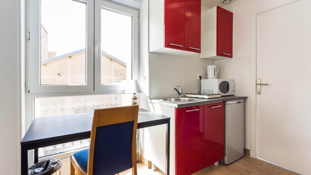 A compact kitchen with a dining area, featuring a window, a sink, a microwave, and red cabinets.