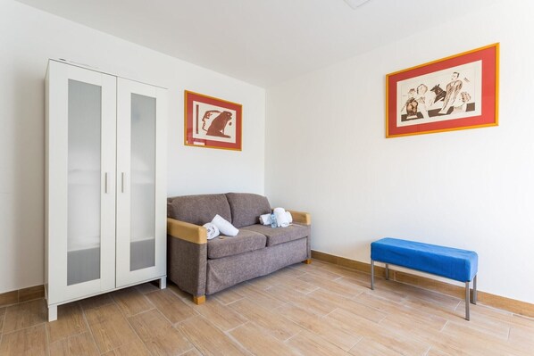 A room with a white wardrobe, a grey sofa, a blue bench, and two framed pictures on the wall.