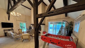 A spacious room with a foosball table, a television, and a large window providing a view of the outdoors. - L'Hydromel, estate with swimming pool 1h30 from Paris (Auvilliers-en-Gâtinais)