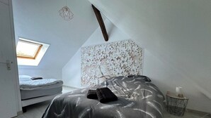 A bedroom with a sloped ceiling, a bed with a black bedspread, a small bedside table with a lamp, and a wall with a floral pattern. - L'Hydromel, estate with swimming pool 1h30 from Paris (Auvilliers-en-Gâtinais)