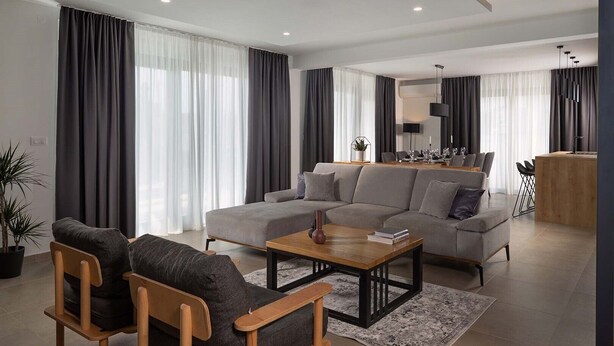A modern living room with a sectional sofa, a coffee table, and a dining area with a kitchen in the background. - Villa Adria in Valbandon (Valbandon)