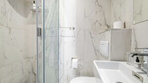Une salle de bain moderne avec une douche à parois de verre, un lavabo blanc et des murs en marbre.