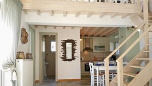 Une cuisine spacieuse avec un plancher en bois, un coin repas avec des chaises blanches et un escalier menant à l’étage supérieur.