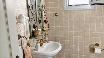 A bathroom with a white sink, a mirror with a decorative frame, a towel hanging on the door, and a window with a view of the outside.