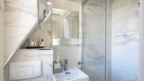 Un bany modern amb una cabina de dutxa de vidre, una paret revestida de marbre, un rentapeus blanc i un mirall damunt del rentapeus.